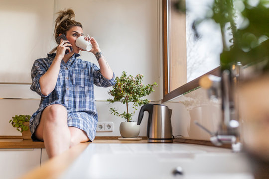beautiful and young woman having breakfast at home and having fun, sitting on the kitchen and talking on the phone