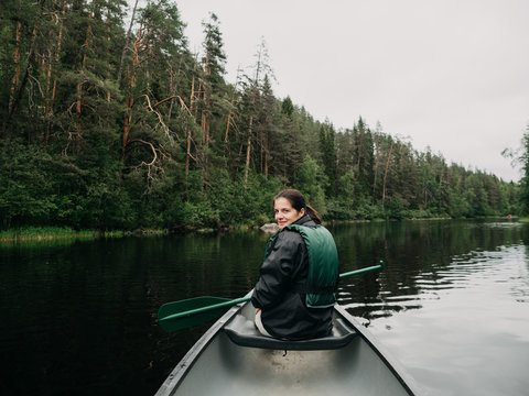 Young smiling woman looking back while boating on forest river in Finland