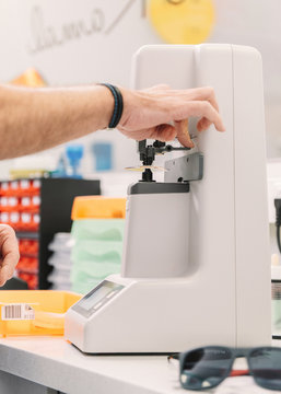 Hands of anonymous optometrist using professional tool to make lens for spectacles in laboratory