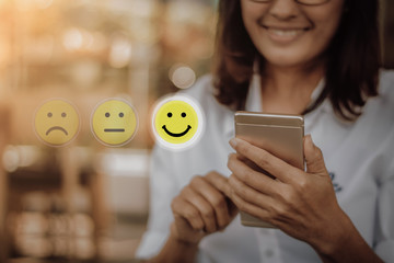 Businesswoman pressing face emoticon on virtual touch screen at smartphone .Customer service...