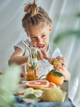 Boy in summer wear with funny hairstyle pressing grapefruit with wooden reamer for juice
