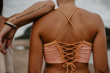 Crop female with tattooed arm leaning on shoulder of unrecognizable friend while spending time on beach together