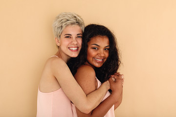 Smiling young caucasian female hugging female friend in studio