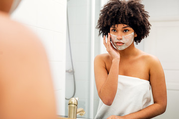 Fototapeta na wymiar Woman applying facial mask in front of bathroom mirror