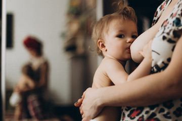 Young beautiful woman is breastfeeding a little baby in a cozy room in home