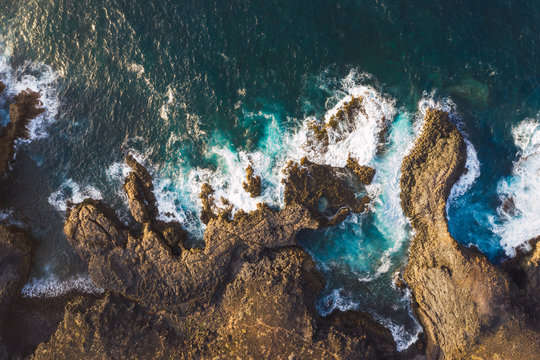 Aerial view of rocky coast in Spain with dashing majestic foamy waves in sunlight