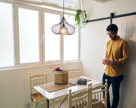 Adult male enjoying fresh hot tea and looking away while sitting at table near knitting needles and yarn