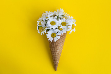 Ice cream cone with chamomiles  in the center of the  yellow background.Top view.Copy space.Spring or summer flowers concept.