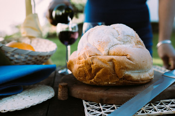 Woman serving red wine in a glass cup, with a bread in the foreground