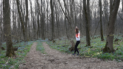 Sporty girl in sportswear walks on slackline in a forest.