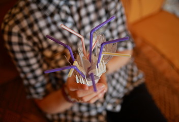 closeup of hands of woman holding white plastic cup with disposable plastic drinking straws, forks inside