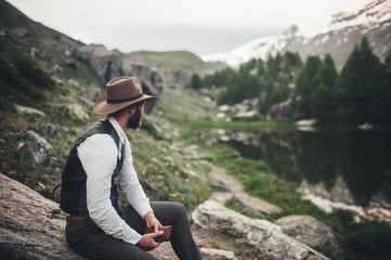 Naklejka premium A man in a hat sits on the lake and looks at the landscape and holds a notebook in his hands