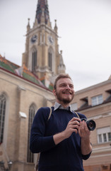 One young man, tourist or traveler holding a photo camera, in a old European style architecture city behind.