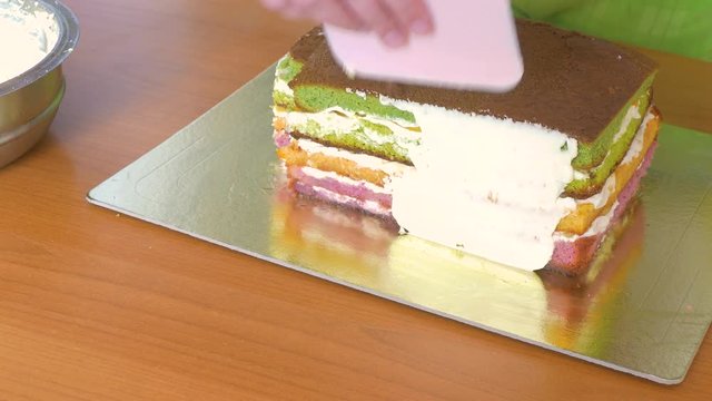 To grease with a cream with a special pastry knife of the side of a sponge cake with multi-colored cake layers