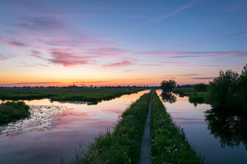 Red sunset over the dutch countryside near the city of Gouda, Holland. A path is leading into the distance between two canals.