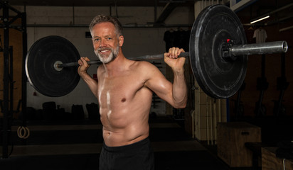 Ein durchtrainierter Mann mittleren Alters macht oberkörperfrei die Übung Clean und Jerk....