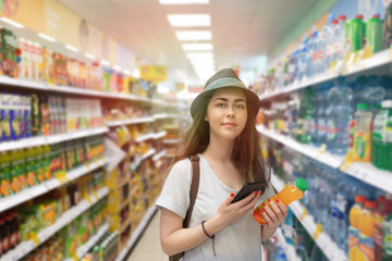 Young beautiful woman chooses a bottle of juice in the supermarket and checks the QR code on the label. The concept of modern technology and shopping in the store. Light
