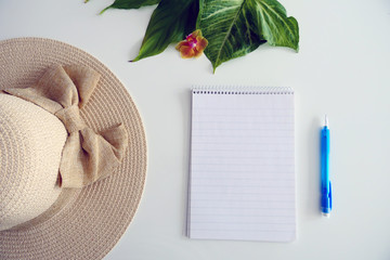 Fresh Green Leaves, Summer Hat, Empty Notebook and a Blue Pen isolated on a White Background
