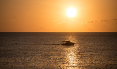 Fototapeta na wymiar Boat sailing at Sunset in the Atlantic Ocean. Fernando de Noronha, northeastern Brazil.