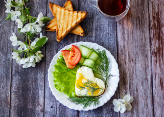 Fried eggs with lettuce, cucumber and tomato slices on wooden background