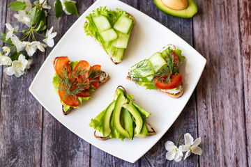Vegetarian sandwiches with avocado, tomatoes and cucumbers on a wooden background