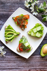 Vegetarian sandwiches with avocado, tomatoes and cucumbers on a wooden background