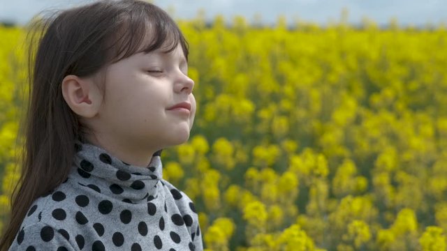 Portrait of a happy child in a field of flowers. Charming little girl in a blooming spring field enjoys the air.