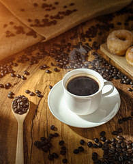 Coffee cup and roasted coffee beans. on wooden background with sunlight.