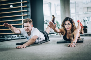 Naklejka premium Attractive fitness woman with coach doing hard exercise in gym