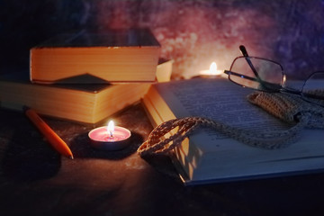 Lighted candles in an intimate setting, old books, yellowed from time to time, glasses in a knitted...