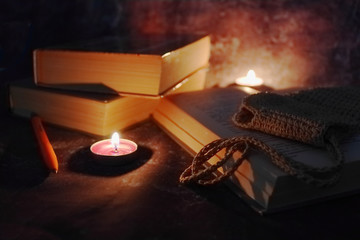 Lighted candles in an intimate setting, old books, yellowed from time to time, glasses in a knitted...