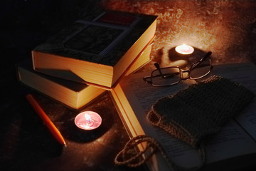 Lighted candles in an intimate setting, old books, yellowed from time to time, glasses in a knitted yellow thread.