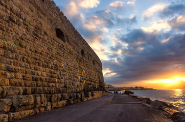 Fortress Koules, Crete - Greece. Beautiful sunset  with colorful cloudy sky at the old Venetian port in Heraklion city. Sun reflections on the sea and the fortress Koules giving them a soft orange hue