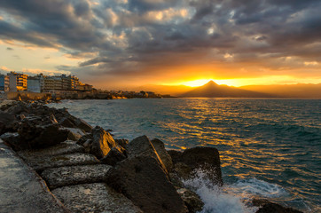 Heraklion, Crete Island - Greece. Colorful sunset with cloudy sky over the sea and the city of Heraklion. Sun is reflected on the sea the rocks and the buildings giving them a soft orange hue