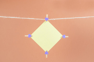 Yellow sticker on clothesline with clothespins isolated on brown background. Place for your text.