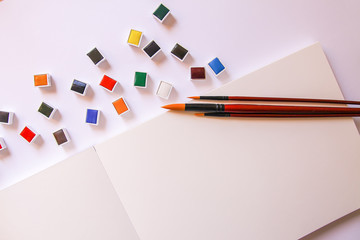 Watercolor paints, brushes and paper on white background. Flat lay, top view