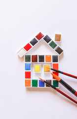 Fototapeta na wymiar Watercolor paints in the shape of a house and paintbrushes on white background. Painting tools. Flat lay, top view