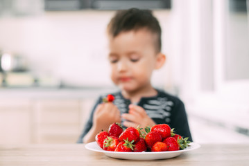 Little boy in the kitchen eating fresh strawberries very appetizing