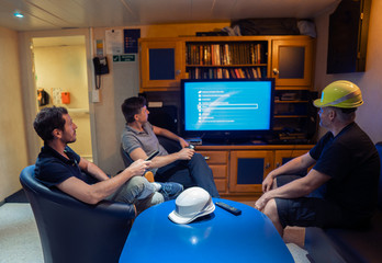 Happy team of ship officers watch TV onboard of vessel. TV, recreation and internet at sea