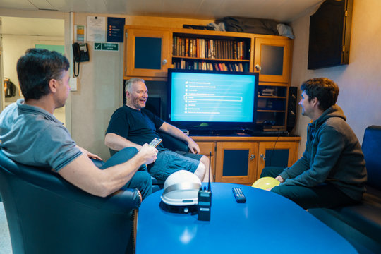 Happy team of ship officers watch TV onboard of vessel. TV, recreation and internet at sea