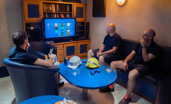 Happy team of ship officers watch TV onboard of vessel. TV, recreation and internet at sea