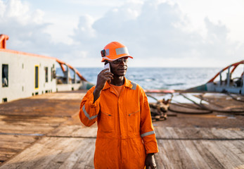 Marine seaman or bosun on deck of vessel or ship . He is speaking on the mobile cell phone