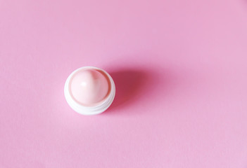 Lip balm in small white plastic container on soft pink background.