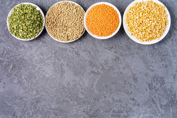 Top view of assortment of peas, lentils, beans and legumes over gray background.