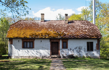 Old house with a moss-covered roof stands in the middle of a derelict garden.