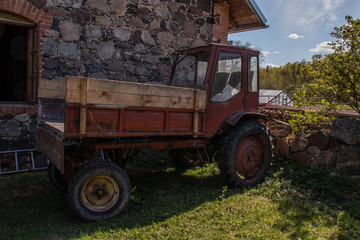 Obraz premium Old red tractor stands near the house with a stone wall