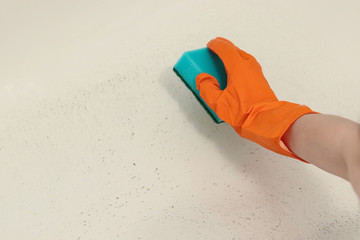 Hand in orange rubber glove, green sponge, dirt on white background