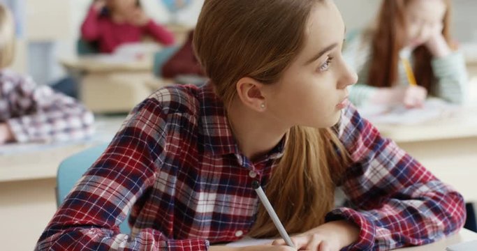 Close up of the Caucasian teen schoolgirl with fair hair writing in the copybook an exercise and thinking at the lesson at the exam.