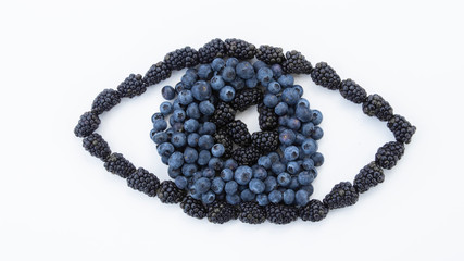 An eye created out of fresh fruit. Resting on a white background with a gleam in the pupil made with blackberries surrounded by fresh blueberries shaping the iris on a white background.