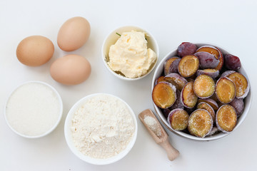 Fototapeta na wymiar Ingredients for plum pie baking on a white background: butter, flour, sugar, baking powder, eggs, frozen plums